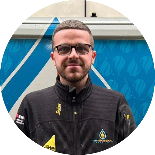 Billy Smith, team member of T.M.S. Mechanical Services, wearing a black work uniform with company logo, standing in front of a branded service van.