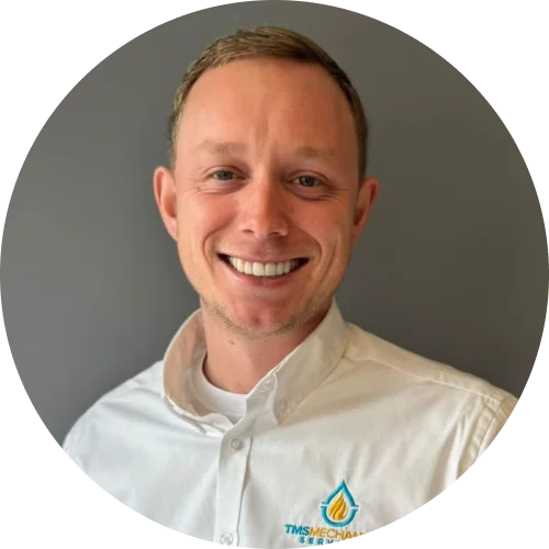 Miles Davies, team member of T.M.S. Mechanical Services, smiling in a company-branded shirt against a neutral background, representing local heating expertise in Essex.
