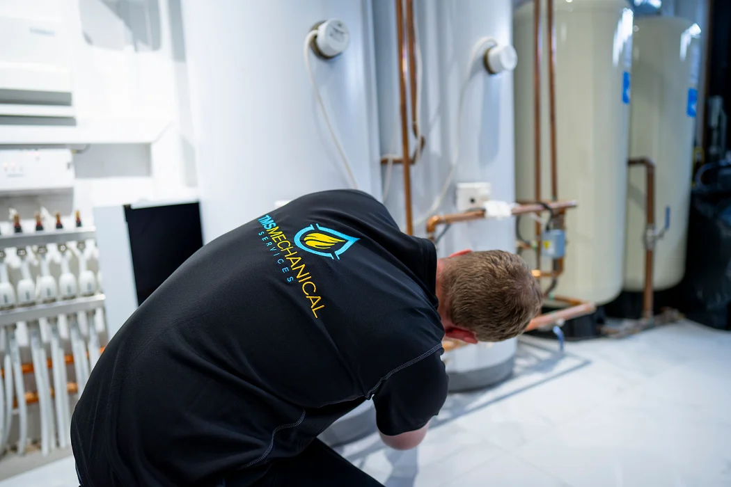 Technician from TMS Mechanical Services working on commercial heating systems, focusing on boiler maintenance and installation in a professional setting.