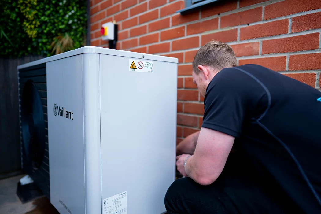 Technician servicing a Vaillant air source heat pump installation outside a brick building, emphasising energy-efficient heating solutions in Hornchurch.