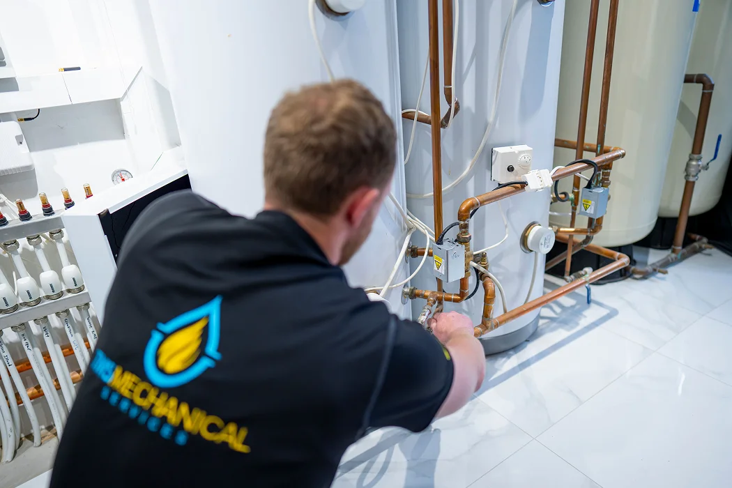 Technician from T.M.S. Mechanical Services adjusting gas piping in a commercial heating system, showcasing expertise in gas mains commissioning and pressure testing.