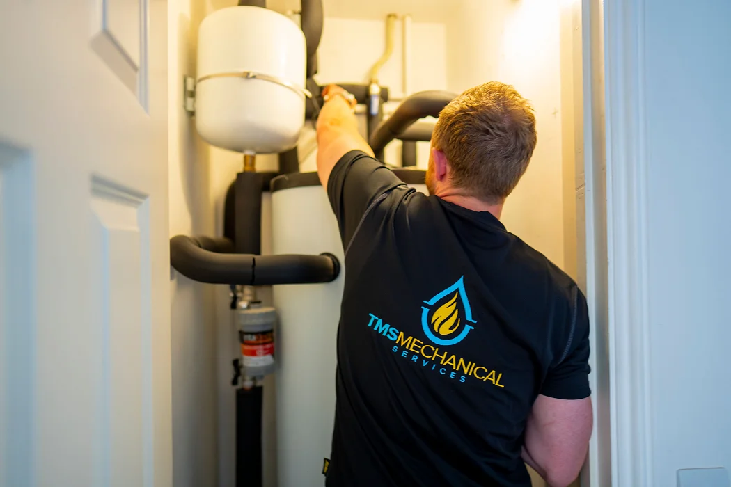 Technician from TMS Mechanical Services adjusting a hot water cylinder installation in a residential setting, showcasing expertise in heating solutions.
