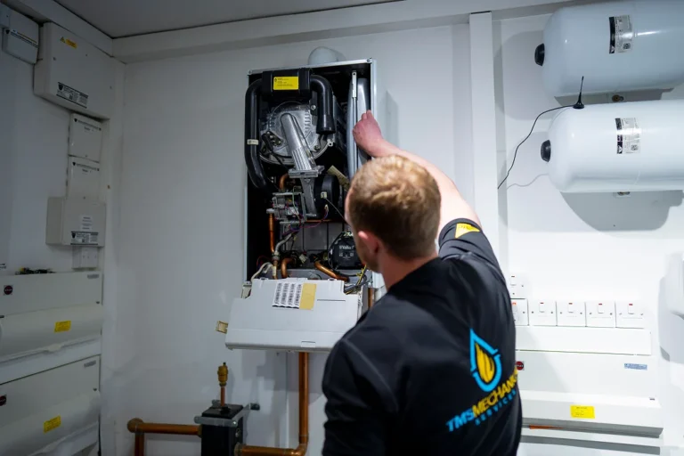 Technician servicing a boiler, showcasing TMS Mechanical Services logo, in a well-equipped heating maintenance environment.