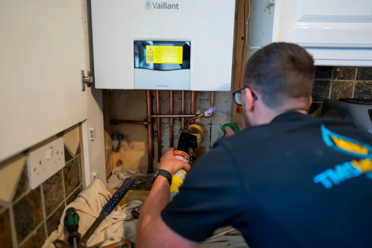 Technician from TMS Mechanical Services performing boiler installation or repair on a Vaillant unit, featuring tools and copper piping in a residential setting.