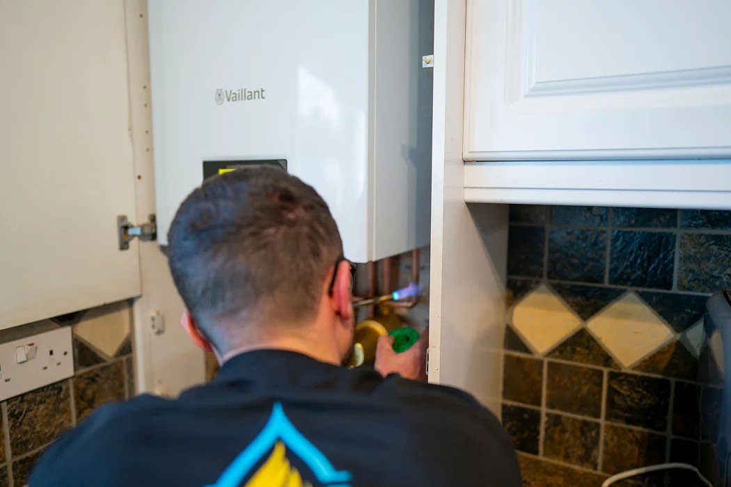 Engineer servicing a Vaillant boiler, adjusting components in a kitchen setting, reflecting T.M.S. Mechanical Services' boiler repair expertise.