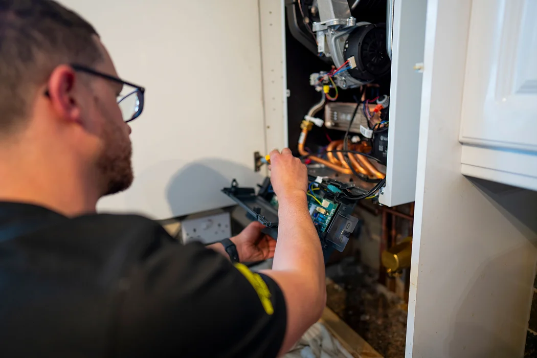 Engineer servicing a gas boiler, inspecting internal components and circuitry for maintenance and repair.